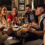 Group of friends are enjoying a meal together. They are talking and laughing while eating their starters and drinking champagne.